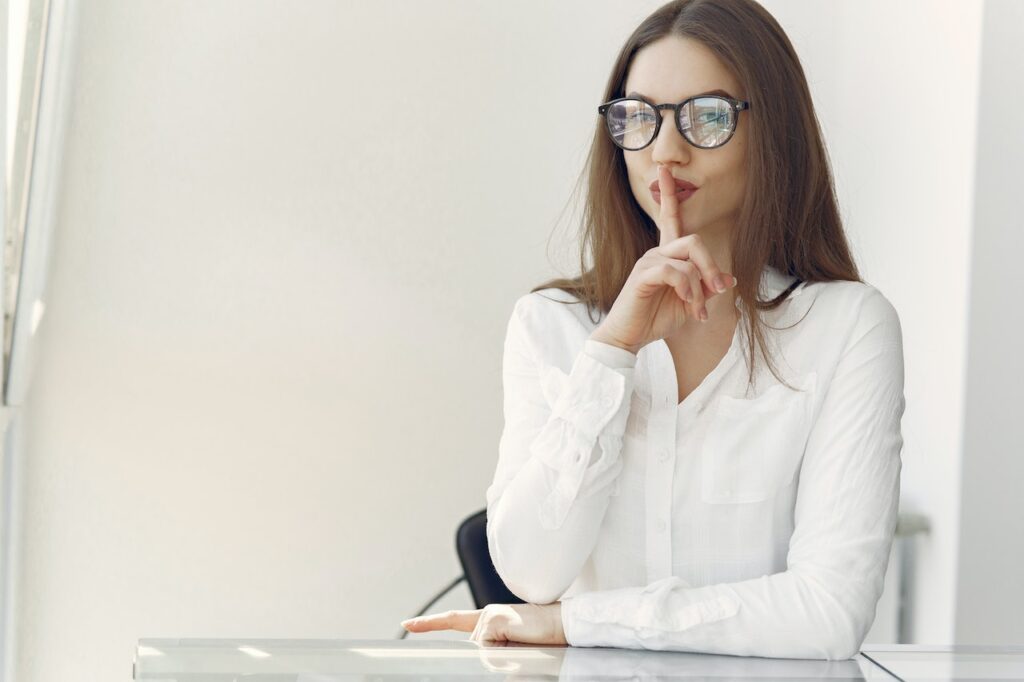 Woman in picture dressed in white clothes holding her finger on her mouht like lying