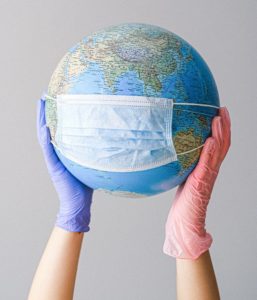 Two hands holding globe that has mask over id alluding to coronavirus