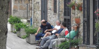 Several older people sitting at the bench in front of the building