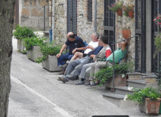 Several older people sitting at the bench in front of the building