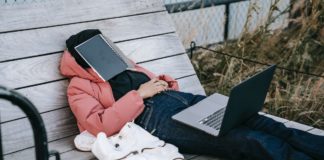 Person laying on bench with laptop on his knees and book on his head dreaming