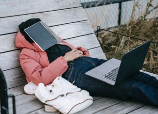 Person laying on bench with laptop on his knees and book on his head dreaming